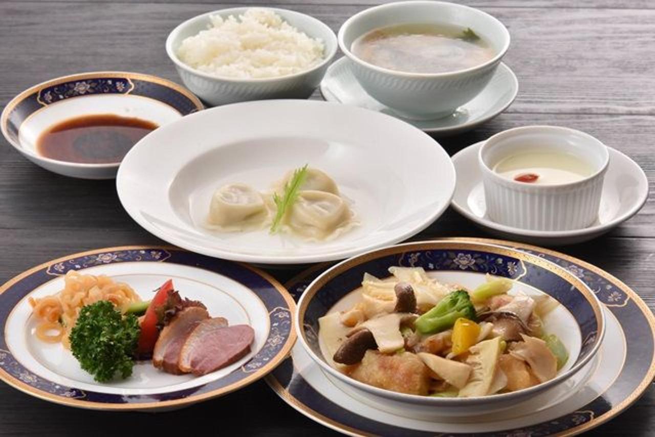 A multi-course meal spread on patterned dark blue and gold-rimmed plates and white dishes, including rice, soup, dumplings, and side vegetables.